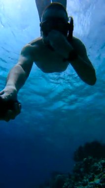 Maldivler 'de su altında şnorkelle yüzen biri diğer eliyle kameraya uzanıp burnunu tutuyor..