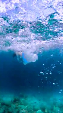 Bir insan Maldivler 'de su altında yüzüyor, renkli bir mayo ve şnorkel yüzgeçleri giyiyor, mercan ve deniz canlılarıyla çevrili..