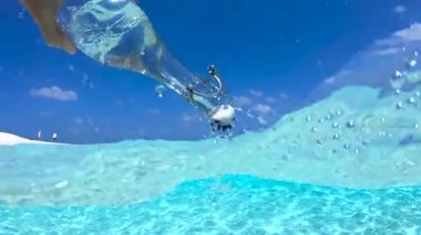 Bora Bora 'da cam şişeyi tutan ve berrak suyun yüzeyine su döken bir el.