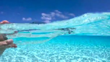 Bir el Maldivler 'in berrak sularına daldırılmış cam bir şişeye uzanır. Parlak bir gökyüzü ve yüzeyde dağılmış bulutlar vardır..