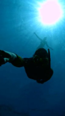 Şnorkeli olan bir dalgıç Raja Ampat Adaları 'nda su altında poz verirken, diğer bir dalgıç ise arka planda güneş ışığıyla aydınlatılıyor..