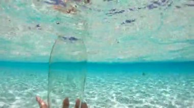 Bora Bora 'daki berrak suyun yüzeyine su döken bir el, canlı mavi ortamı ve kumlu arkaplanı gözler önüne seriyor.