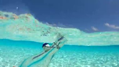 Bora Bora 'daki bir sualtı sahnesinde cam bir şişe kristal berraklığında suya batırılmış, yukarıdaki kumlu taban ve mavi gökyüzünü gösteriyor..