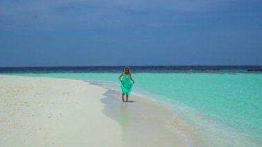 Kadın Maldivler 'de kumlu bir sahil boyunca yürüyor, okyanus dalgaları yavaşça ayaklarına vuruyor..