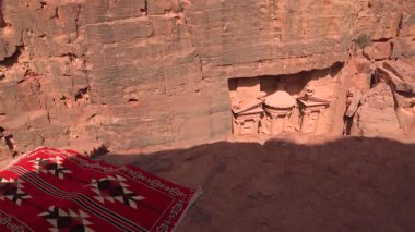 Ürdün, Petra 'da, ön planda kırmızı desenli bir halı ile kayalık bir yüze oyulmuş eski Hazine' nin yukarıdan görünüşü.