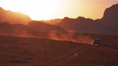 Arabalar, gün batımında toz izlerini tekmeleyen kırmızı kum çölünden geçer ya da Ürdün Wadi Rum 'daki kaya oluşumları arasında gün doğumunu takip eder..