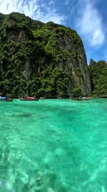 Uzun kuyruklu botlar yeşil ağaçlarla kaplı kayalık adaların yakınında turkuaz sularda yüzerler. Gökyüzü beyaz bulutlarla mavidir. Seyahat temaları, tatil reklamları veya hedef pazarlama için elverişli.