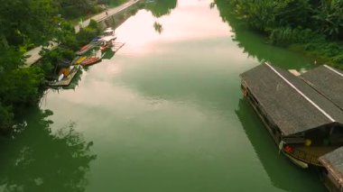 Dar bir Amazon Nehri kanalı, sazdan yapılar, botlar ve tropikal bitki örtüsünün ortasındaki nehir kıyısındaki insanlar..