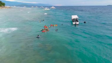 Yüzen ve şnorkelle yüzen bir grup insanın tropik bir sahil şeridi olan Boracay, Filipinler 'de kıyıya demir atmış birkaç tekneyle birlikte hava görüntüsü..