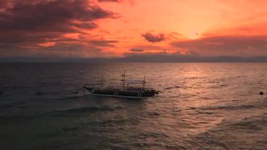 Geleneksel Filipinliler, uzak adaları Boracay, Filipinler 'de canlı turuncu ve kırmızı günbatımında okyanusta yüzen tekneleri kullanırlar..