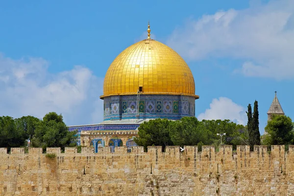 The photo shows the iconic golden dome of the rock, a holy site located in the Old City of Jerusalem, Israel. The dome is made of shimmering gold and features intricate patterns and designs, standing out against a blue sky.