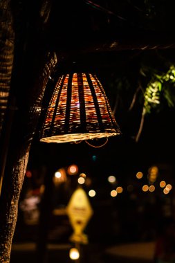 Ağaçtan sarkan, bambu şeritlerden yapılmış ağ tipi sepetle kaplı bir ışık ve arka planda güzel bir bokeh..