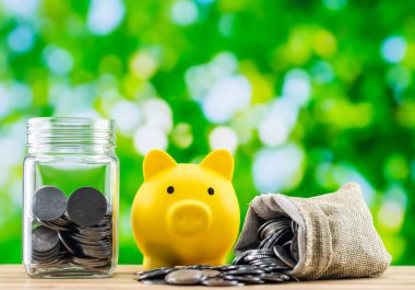 A glass jar and a yellow piggy bank along with a sack full of coins. clipart