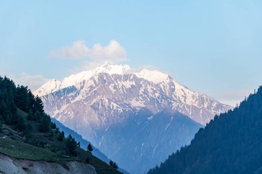 Gün batımında arka planda mavi gökyüzü olan karlı dağ zirvesi.