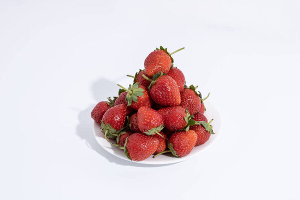 handful of strawberries on a white plate on a white background