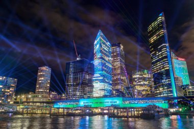Sydney, Avustralya. Sydney Limanı 'ndan şehrin silueti. Binalar ve gökyüzü renkli ışıklar ve yıllık canlı Sydney festivali için projektörlerle aydınlanıyor. 3 Haziran. 2024