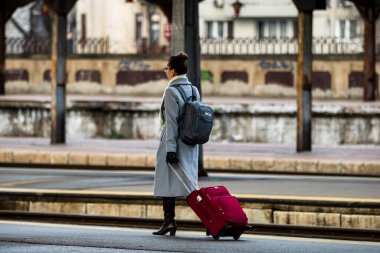 Tourist pulling luggage. Commuters walking at railroad station platform in Bucharest, Romania, 2022
