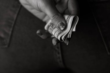 Kadın eli kot pantolonunun arka cebinden para alıyor. Kadın arkasında para saklıyor. Dolarlık banknotlar kapanıyor