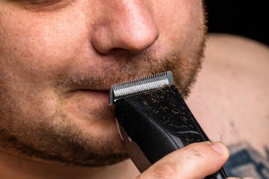 Adam saç makası kullanarak sakalını tıraş ediyor ya da kesiyor.