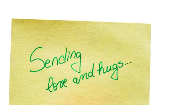 Sending love and hugs handwriting text close up isolated on yellow paper with copy space.