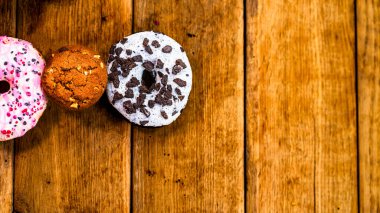 Ahşap masada renkli çörekler. Jöleli şekerli tatlı yiyecekler, çikolatalı donutlar. Kopyalama alanı olan üst görünüm