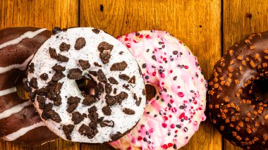 Ahşap masada renkli çörekler. Jöleli şekerli tatlı yiyecekler, çikolatalı donutlar. Kopyalama alanı olan üst görünüm
