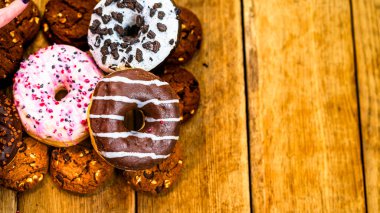 Ahşap masada renkli çörekler. Jöleli şekerli tatlı yiyecekler, çikolatalı donutlar. Kopyalama alanı olan üst görünüm