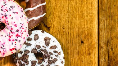 Ahşap masada renkli çörekler. Jöleli şekerli tatlı yiyecekler, çikolatalı donutlar. Kopyalama alanı olan üst görünüm