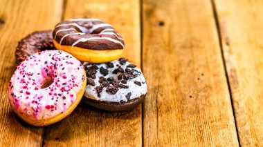 Ahşap masada renkli çörekler. Jöleli şekerli tatlı yiyecekler, çikolatalı donutlar. Kopyalama alanı olan üst görünüm