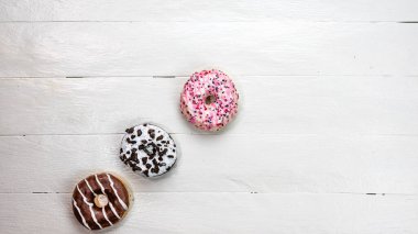 Beyaz ahşap masada renkli çörekler. Şekerli, şekerli, şekerli, şekerli, şekerli. Kopyalama alanı olan üst görünüm