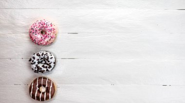 Beyaz ahşap masada renkli çörekler. Şekerli, şekerli, şekerli, şekerli, şekerli. Kopyalama alanı olan üst görünüm