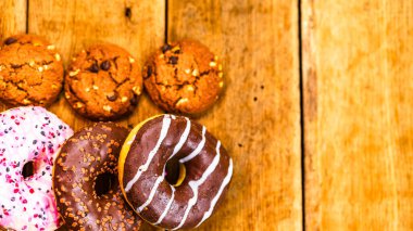 Ahşap masada renkli çörekler. Jöleli şekerli tatlı yiyecekler, çikolatalı donutlar. Kopyalama alanı olan üst görünüm