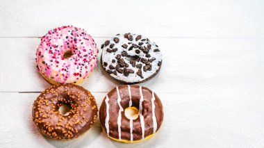 Beyaz ahşap masada renkli çörekler. Şekerli, şekerli, şekerli, şekerli, şekerli. Kopyalama alanı olan üst görünüm