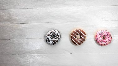 Beyaz ahşap masada renkli çörekler. Şekerli, şekerli, şekerli, şekerli, şekerli. Kopyalama alanı olan üst görünüm