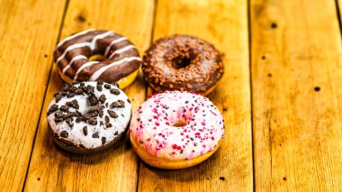 Ahşap masada renkli çörekler. Jöleli şekerli tatlı yiyecekler, çikolatalı donutlar. Kopyalama alanı olan üst görünüm