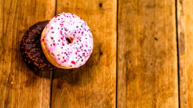 Ahşap masada renkli çörekler. Jöleli şekerli tatlı yiyecekler, çikolatalı donutlar. Kopyalama alanı olan üst görünüm