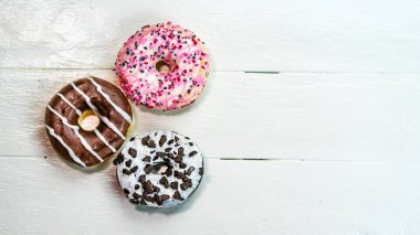 Beyaz ahşap masada renkli çörekler. Şekerli, şekerli, şekerli, şekerli, şekerli. Kopyalama alanı olan üst görünüm