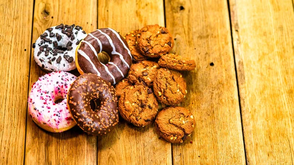 Ahşap masada renkli çörekler ve bisküviler. Jöleli şekerli tatlı yiyecekler, çikolatalı donutlar. Kopyalama alanı olan üst görünüm