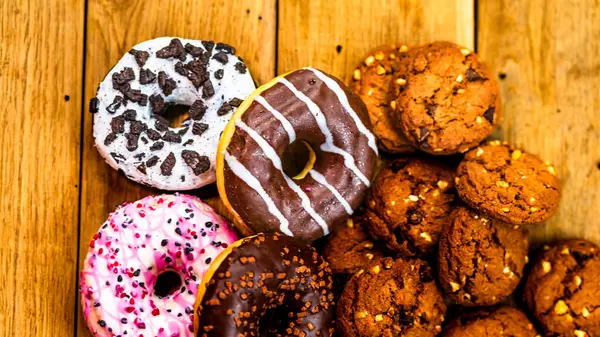 Ahşap masada renkli çörekler ve bisküviler. Jöleli şekerli tatlı yiyecekler, çikolatalı donutlar. Kopyalama alanı olan üst görünüm