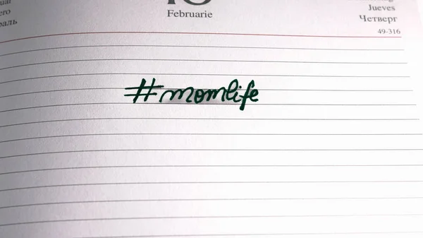 Mother`s day concept. Writing text for mother on personal agenda. Hashtag momlife.