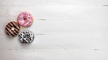 Beyaz ahşap masada renkli çörekler. Şekerli, şekerli, şekerli, şekerli, şekerli. Kopyalama alanı olan üst görünüm