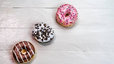 Beyaz ahşap masada renkli çörekler. Şekerli, şekerli, şekerli, şekerli, şekerli. Kopyalama alanı olan üst görünüm