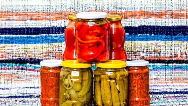 Glass jars with pickled red bell peppers and pickled cucumbers (pickles) isolated. Jars with variety of pickled and canned vegetables. Preserved food concept in a rustic composition.