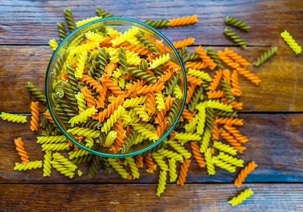 Composition of raw pasta uncooked tricolore fusilli, pasta twist shape. Close up and selective focus on colorful fusilli pasta. Fusilli pasta in bowl.