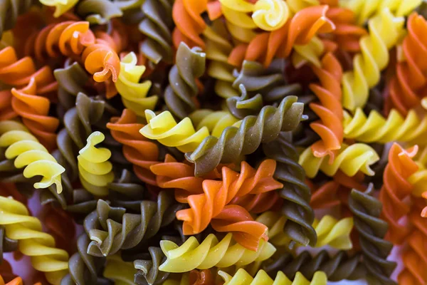 Composition of raw pasta uncooked tricolore fusilli, pasta twist shape. Close up and selective focus on colorful fusilli pasta.