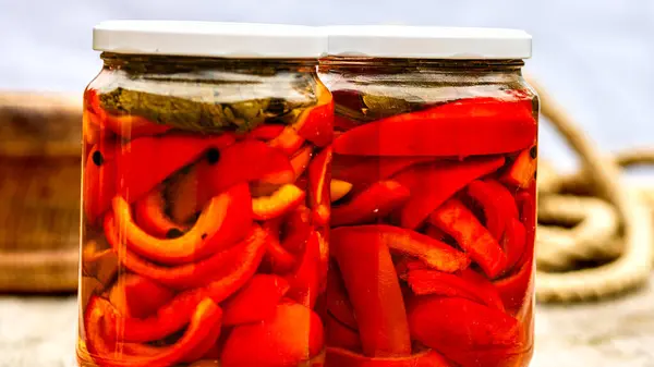 Glass jars with pickled red bell peppers.Preserved food concept, canned vegetables isolated in a rustic composition.