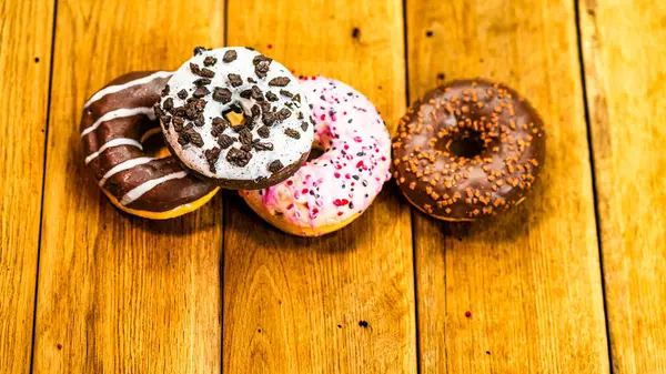 Ahşap masada renkli çörekler. Jöleli şekerli tatlı yiyecekler, çikolatalı donutlar. Kopyalama alanı olan üst görünüm