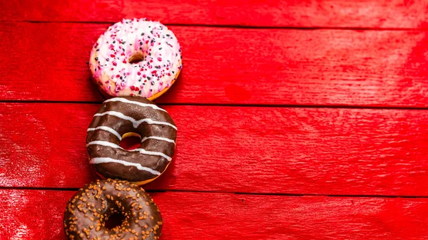 Colorful donuts on red wooden table. Sweet icing sugar food with glazed sprinkles, doughnut with chocolate frosting. Top view with copy space