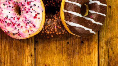Ahşap masada renkli çörekler. Jöleli şekerli tatlı yiyecekler, çikolatalı donutlar. Kopyalama alanı olan üst görünüm