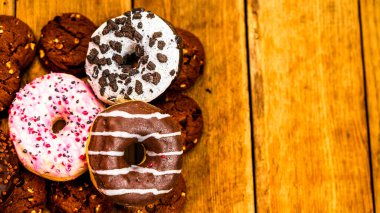 Ahşap masada renkli çörekler. Jöleli şekerli tatlı yiyecekler, çikolatalı donutlar. Kopyalama alanı olan üst görünüm